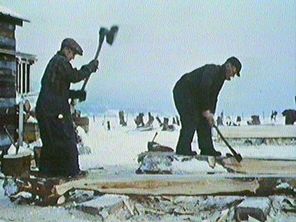 A still from the NFB film "jean Richard" showing workers using adzes to shape the timbers for the ship's hull.